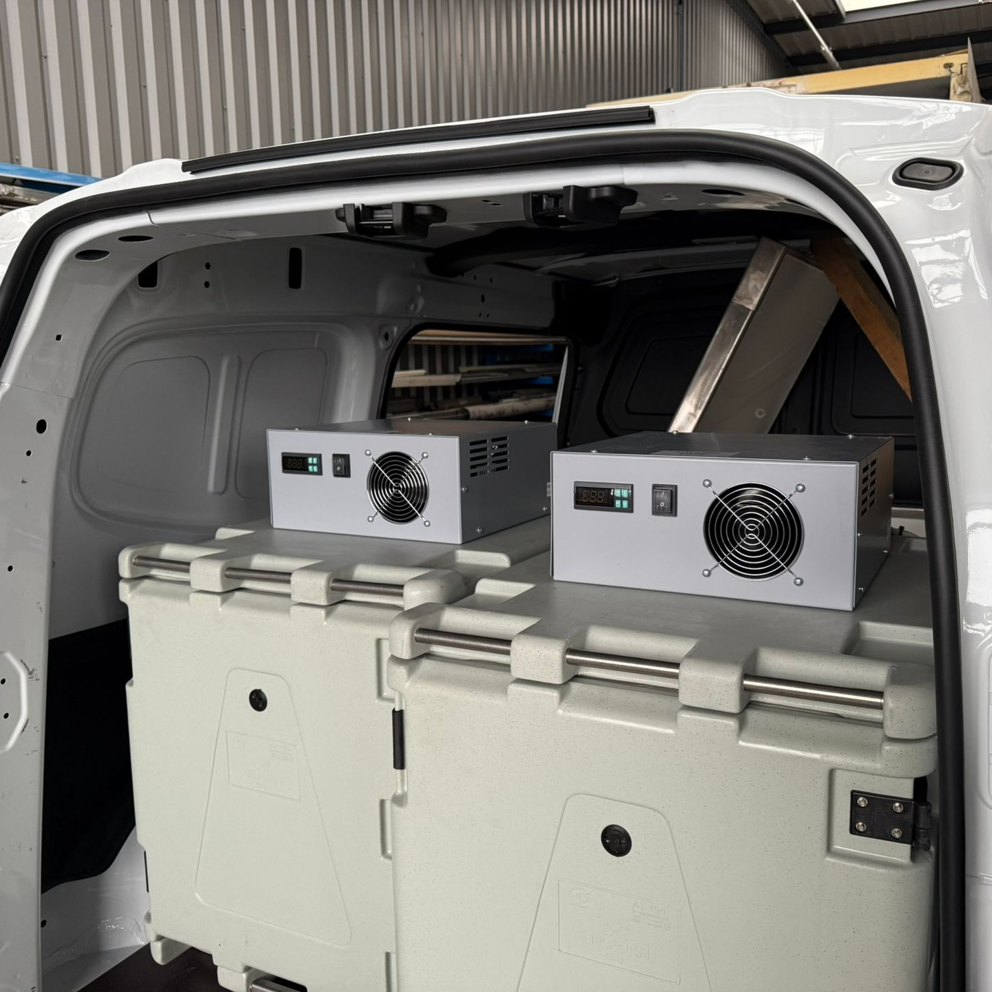 À l'intérieur d'une camionnette blanche : deux unités électroniques grises, posées sur des conteneurs isothermes blancs.