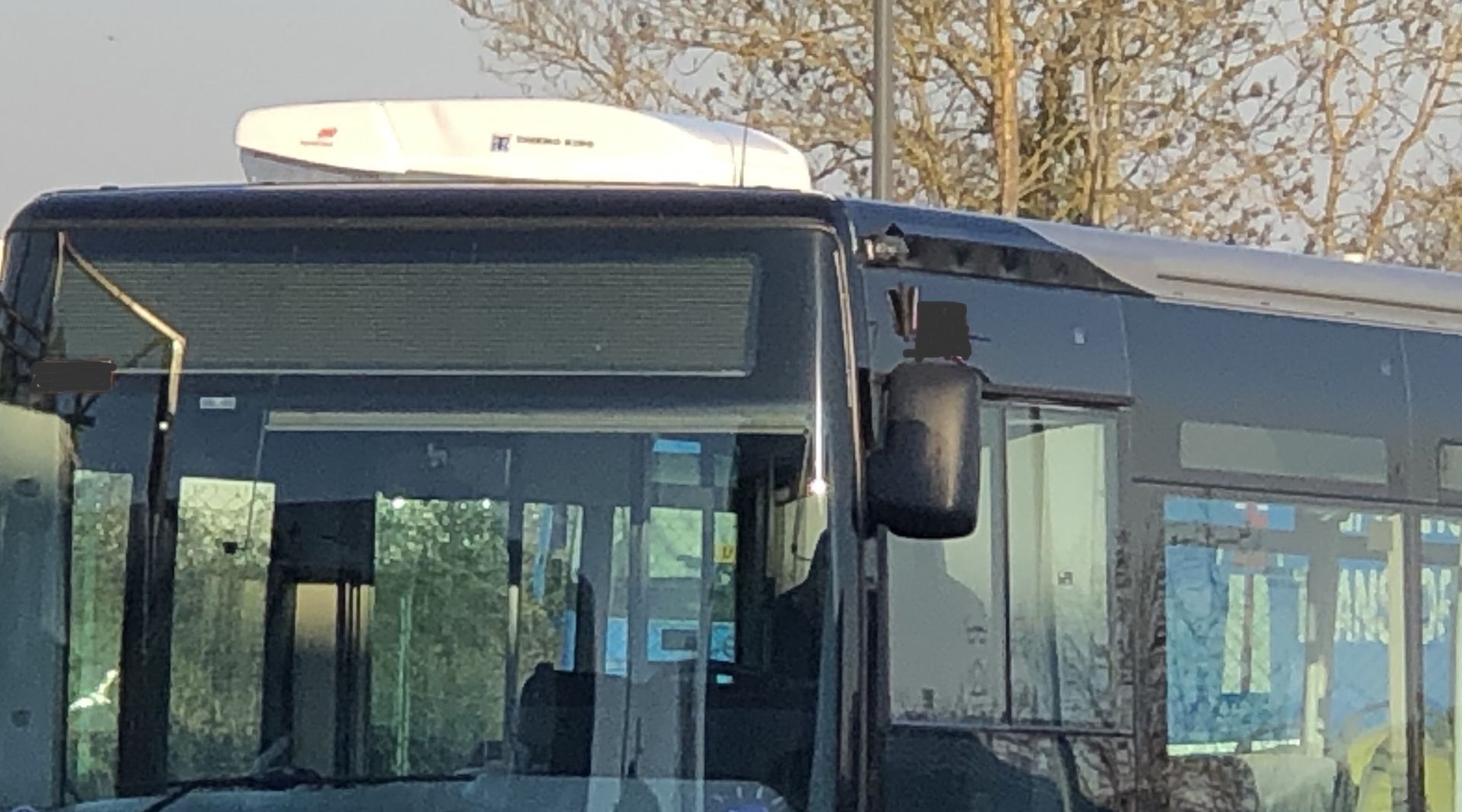 Un climatiseur sur le toit d'un véhicule clair, avec des finitions noires et une camionnette blanche en arrière-plan.