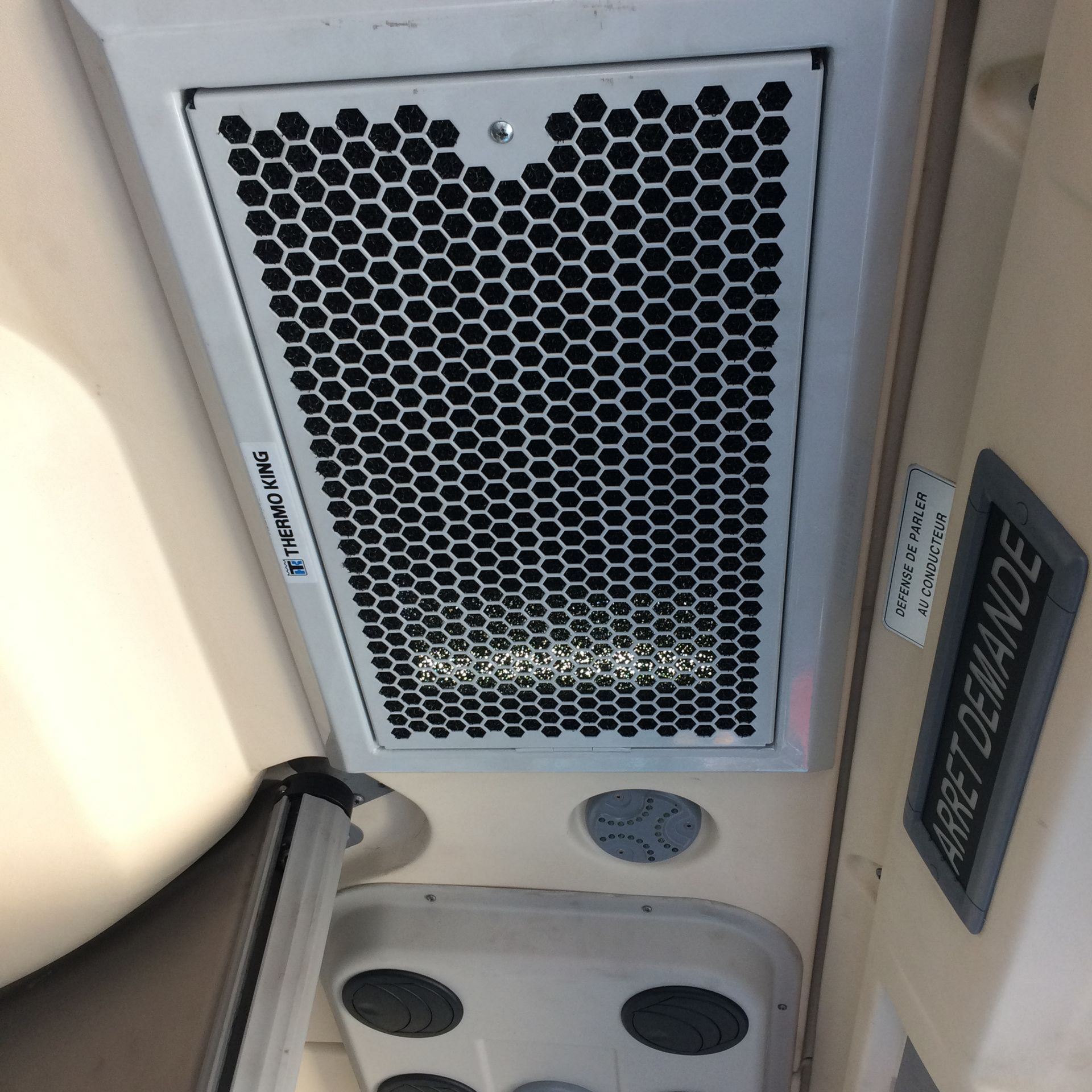 Le plafond d'un bus avec grille d'aération en nid d'abeille et panneau Arrêt demandé.