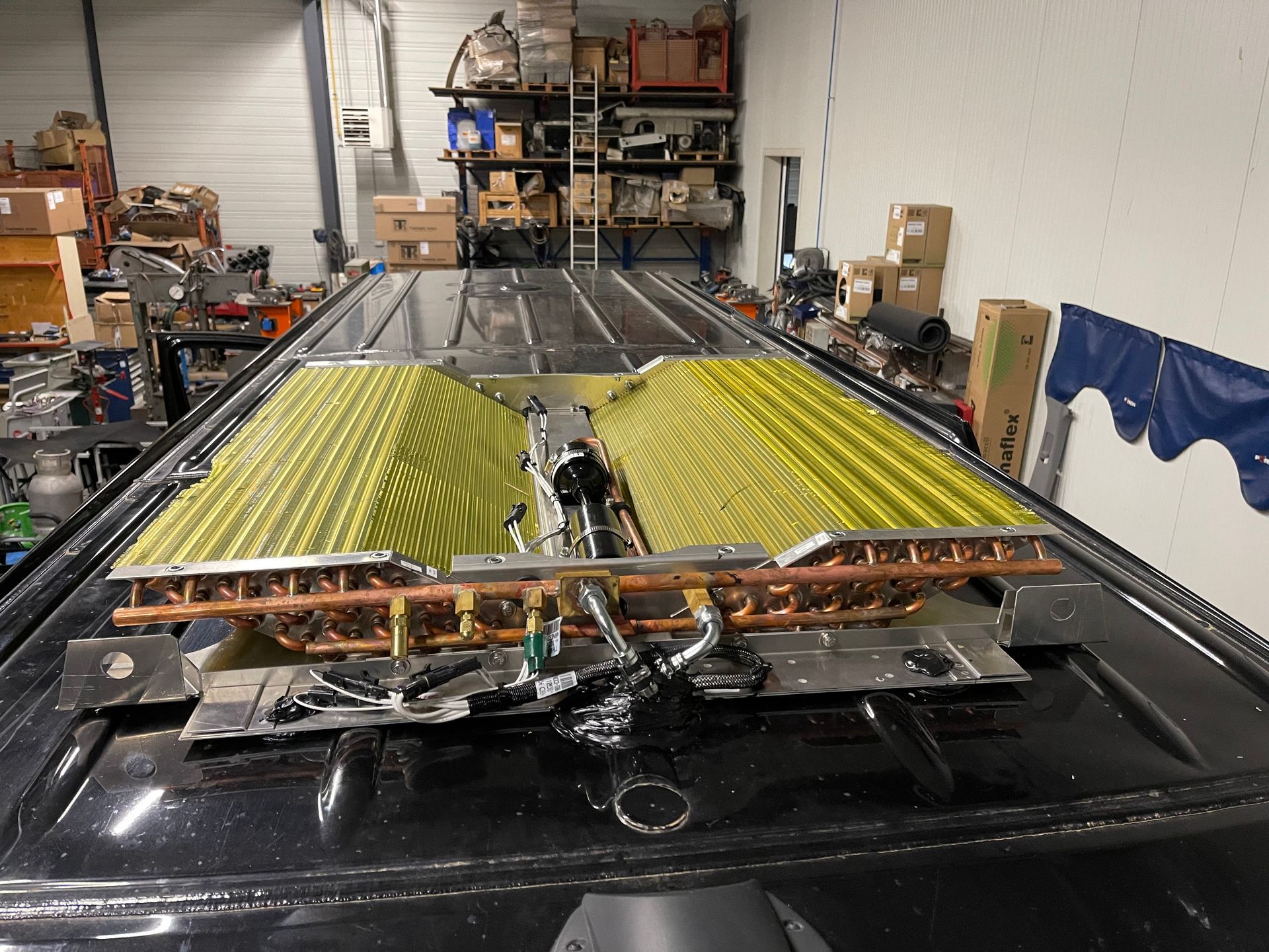 Toit de fourgonnette avec serpentins enveloppés de jaune et tubes de cuivre installés, probablement partie d'un système de chauffage, ventilation et climatisation, dans un atelier.