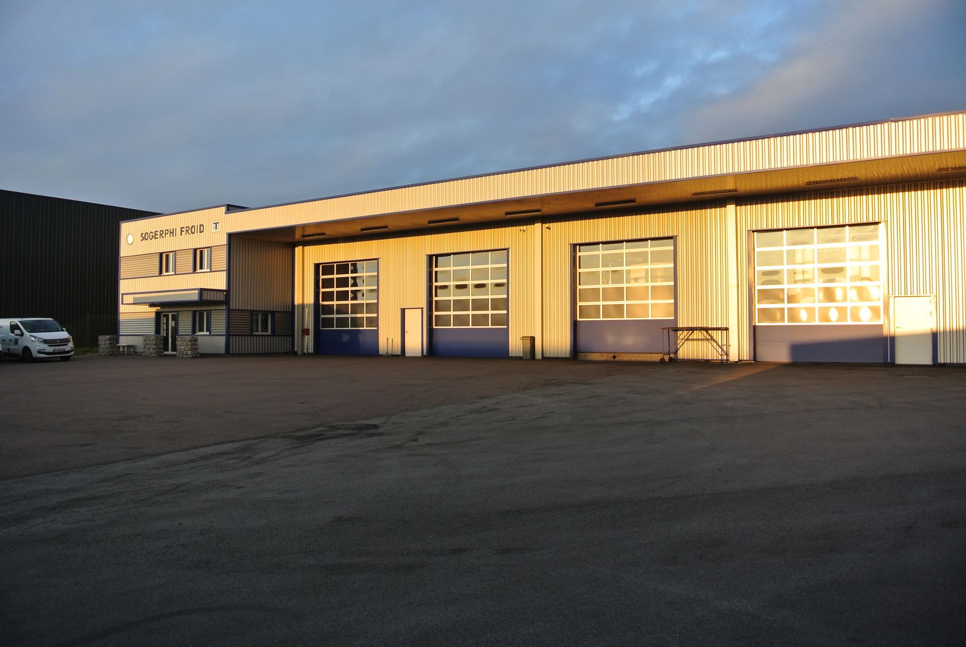 Bâtiment avec portes de garage, terrain pavé, ciel nuageux.