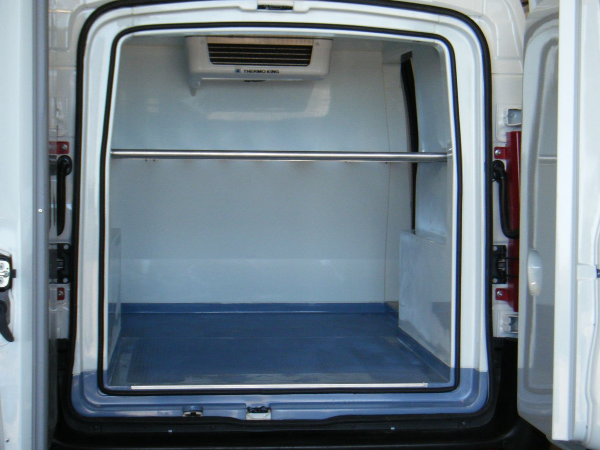 Vue intérieure d'une camionnette frigorifique blanche avec sol bleu, étagère métallique et groupe frigorifique au plafond.