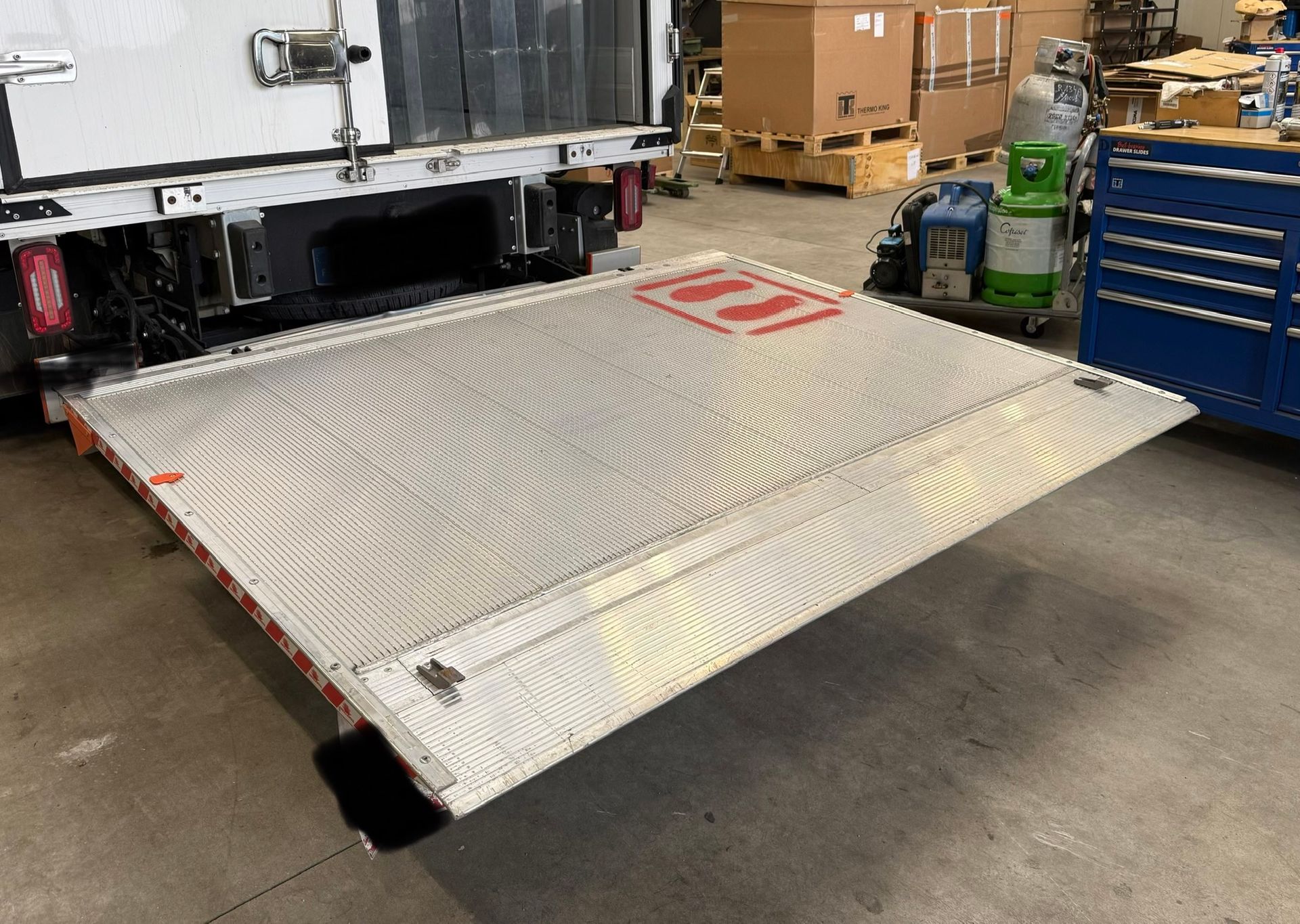 Camion équipé d'un hayon élévateur argenté allongé ; étiquette d'avertissement rouge.