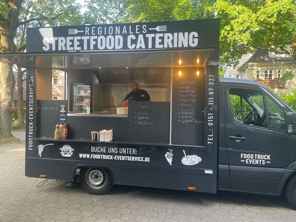 Ein schwarzer Imbisswagen mit der Aufschrift „Regionales Streetfood Catering“ steht am Straßenrand.