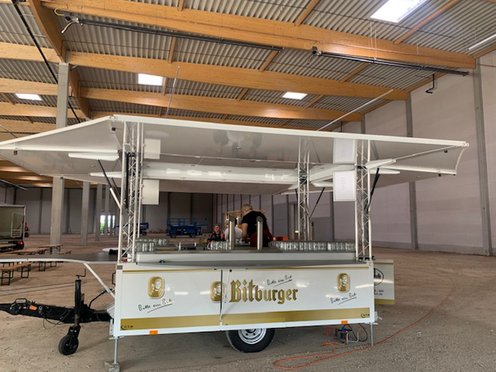 Ein weißer Anhänger mit der Aufschrift „Bitburger“ steht in einer Lagerhalle.