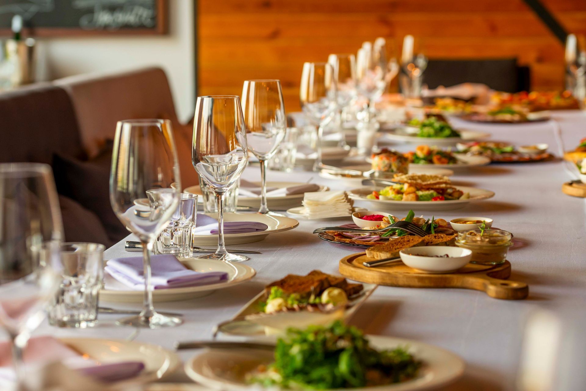 Ein langer, für eine Mahlzeit gedeckter Tisch mit Tellern, Gläsern und Besteck in einem Restaurant.