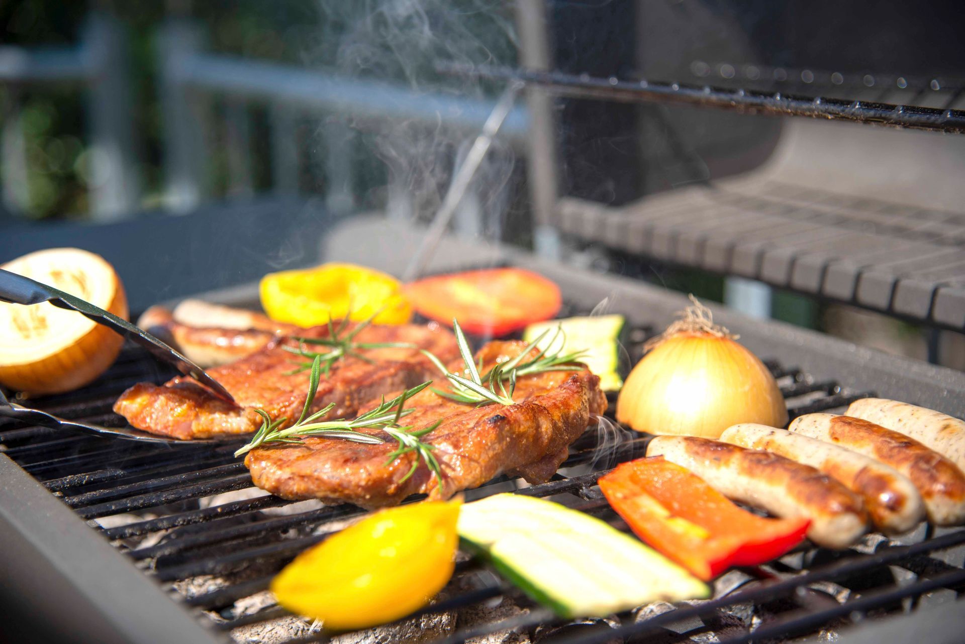 Eine Person bereitet Fleisch und Gemüse auf einem Grill zu.