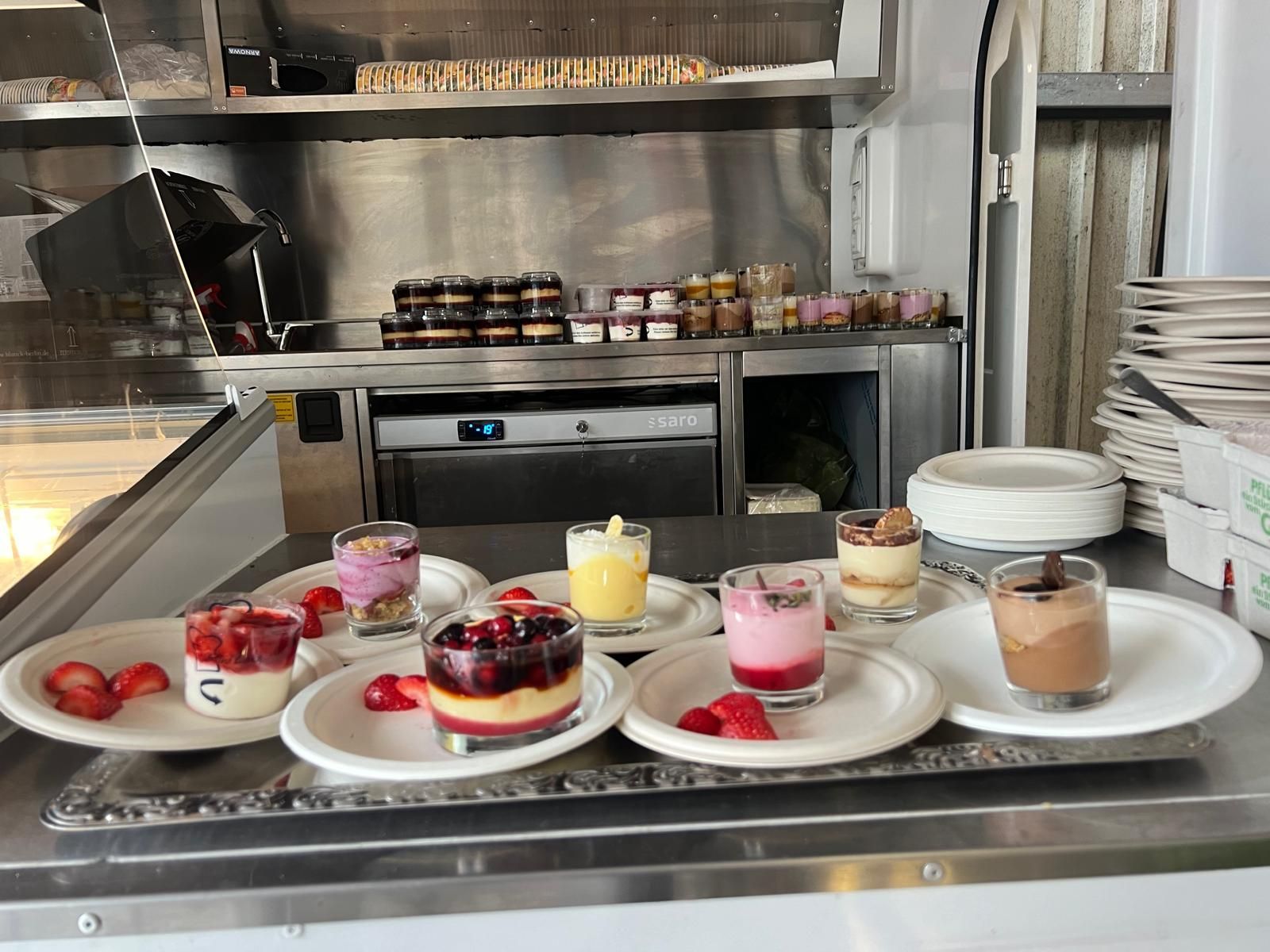 Eine Auswahl an einzelnen Dessertbechern mit Frucht- und Sahnehaube auf weißen Tellern, arrangiert auf einem metallenen Präsentationsständer.