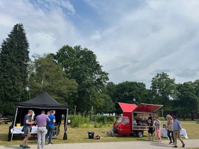 Eine Gruppe von Menschen steht in einem Park um einen Imbisswagen herum.