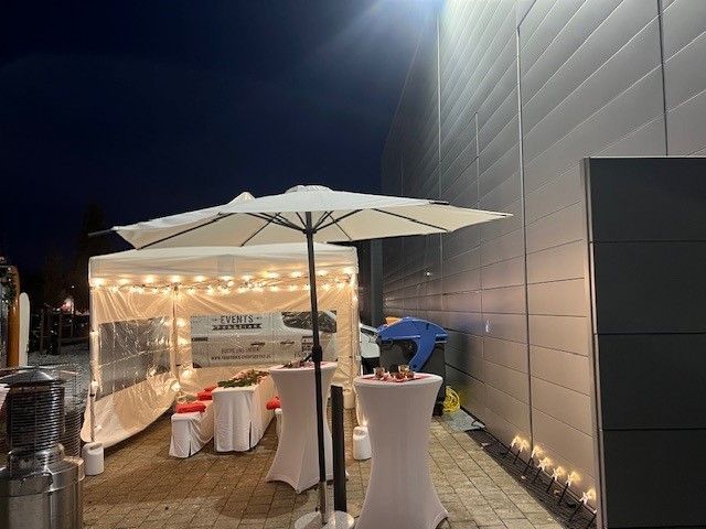 Ein Zelt mit Tischen und Sonnenschirmen vor einem Gebäude bei Nacht.