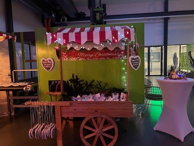 Ein Holzkarren mit einer rot-weißen Markise und einem Schild mit der Aufschrift „Frohe Weihnachten“