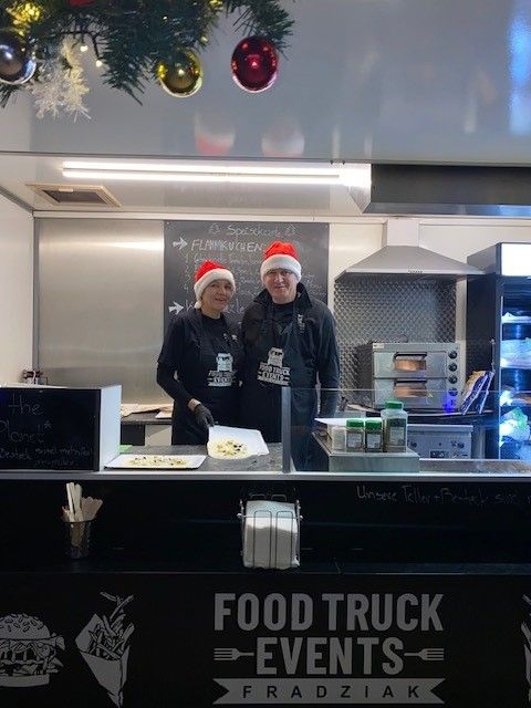 Zwei Personen stehen hinter einer Theke mit der Aufschrift „Food Truck Events“