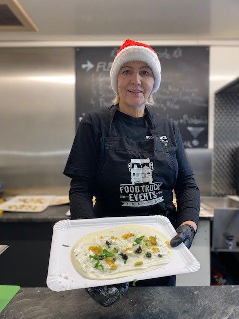 Eine Frau mit Weihnachtsmannmütze hält eine Pizza auf einem Tablett.