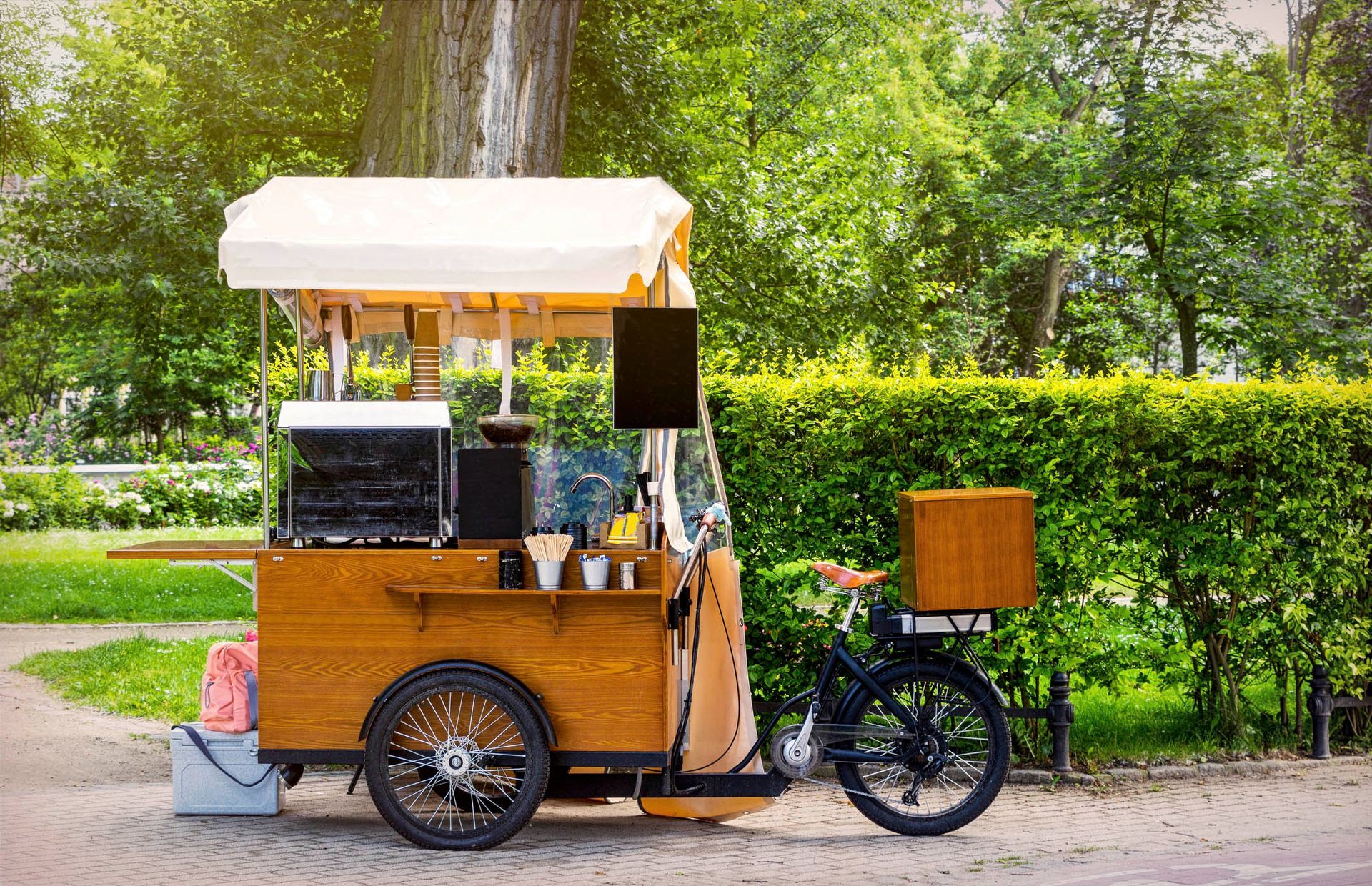 In einem Park steht ein Imbisswagen aus Holz mit einem daran befestigten Fahrrad.