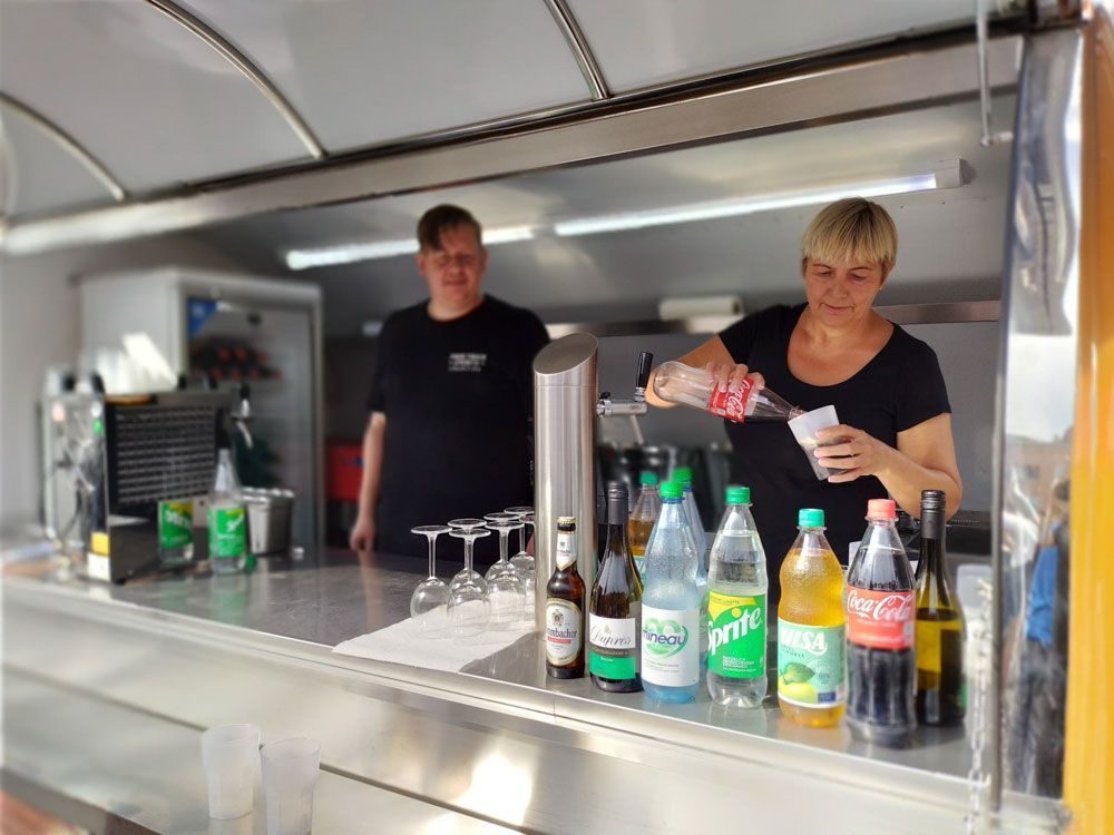 Eine Frau gießt ein Getränk in ein Glas, während ein Mann hinter ihr steht