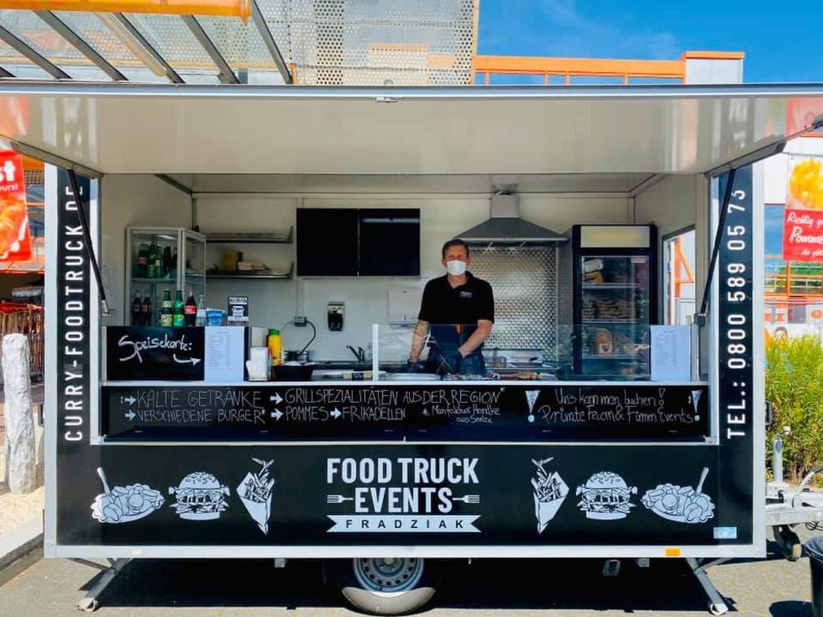 Ein Mann mit einer Maske steht vor einem Imbisswagen.