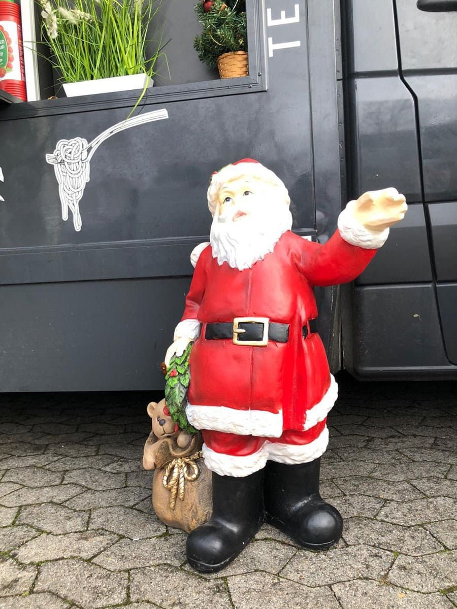 Eine Statue des Weihnachtsmannes steht vor einem schwarzen Lieferwagen