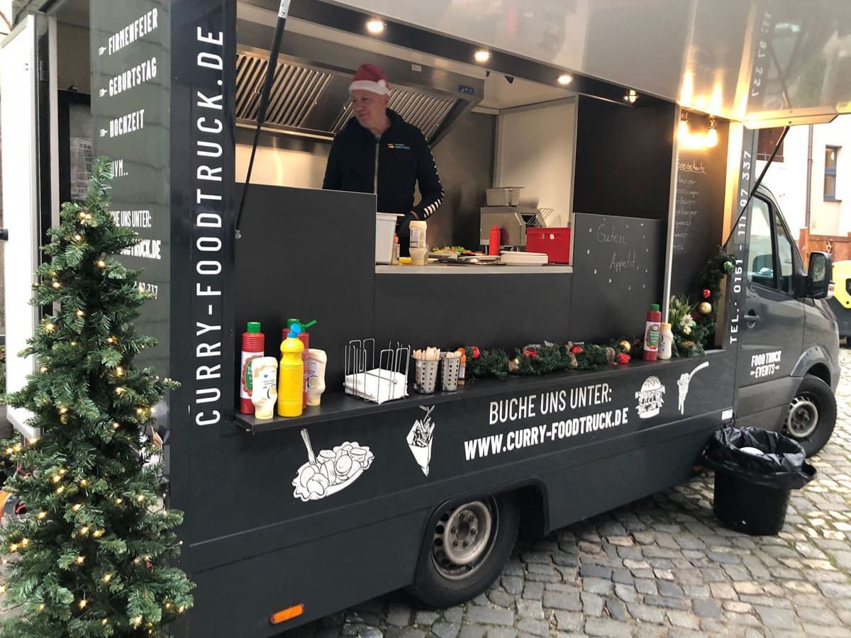 Ein Curry-Imbisswagen parkt auf einer Kopfsteinpflasterstraße neben einem Weihnachtsbaum.
