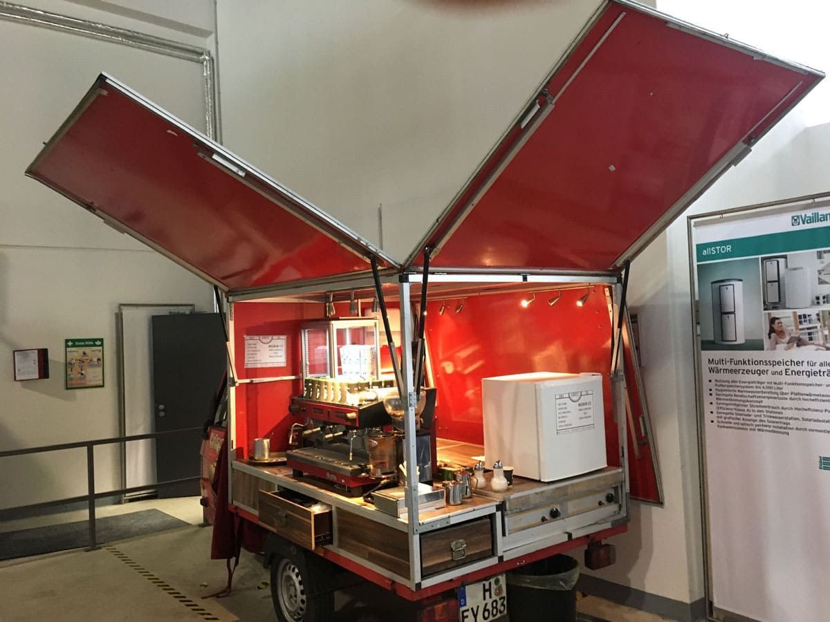 Ein rot-weißer Imbisswagen steht mit offenen Türen in einem Raum.