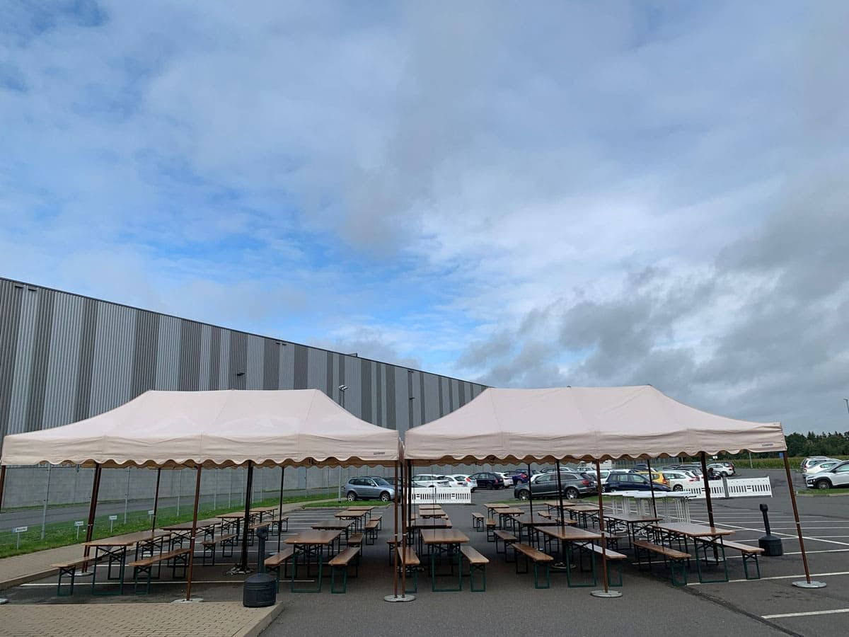 Eine Reihe von Zelten mit Tischen darunter auf einem Parkplatz.