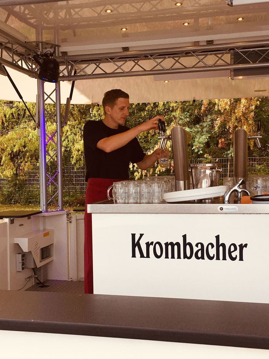 Ein Mann steht hinter einer Theke mit der Aufschrift „Krombacher“