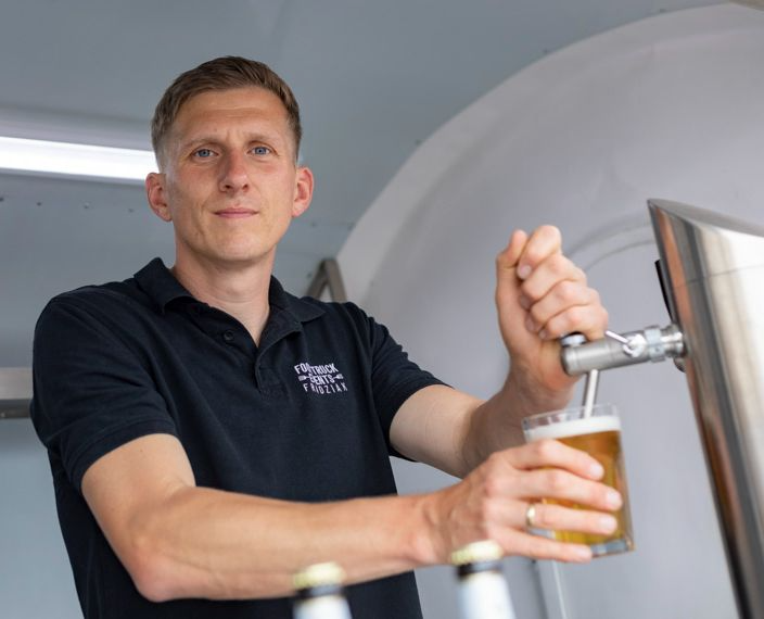 Ein Mann in einem schwarzen Hemd gießt Bier in ein Glas