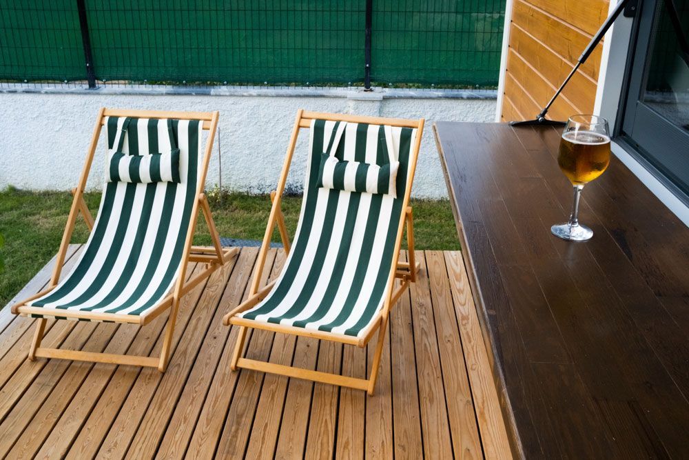 Zwei Gartenstühle stehen auf einer Holzterrasse neben einem Glas Bier.