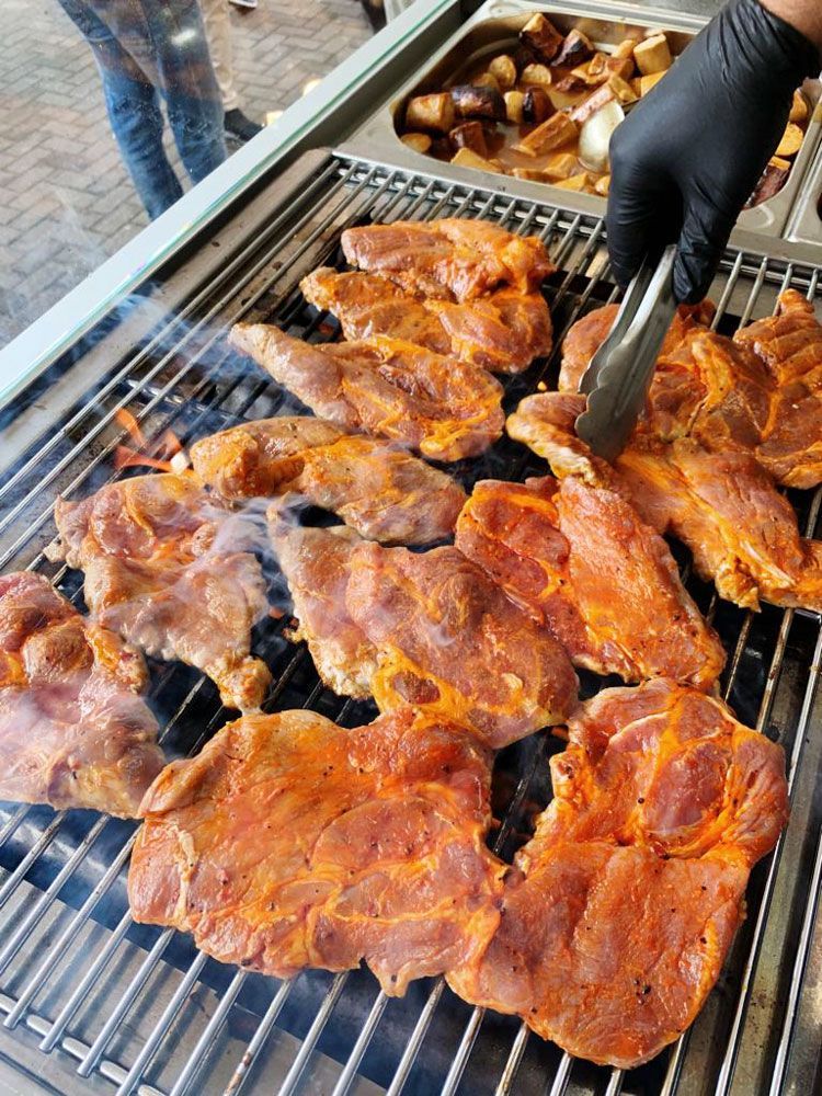 Eine Person grillt mit einer Zange Fleisch auf einem Grill.