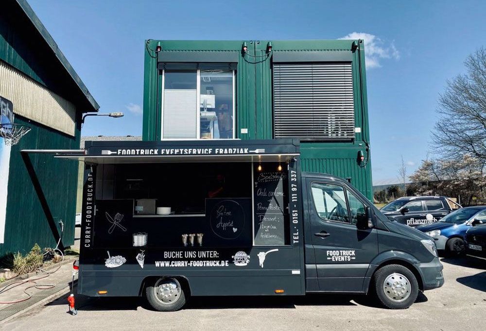 Vor einem grünen Gebäude parkt ein Imbisswagen.