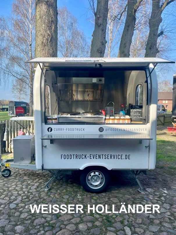 Vor Bäumen parkt ein weißer Imbisswagen.
