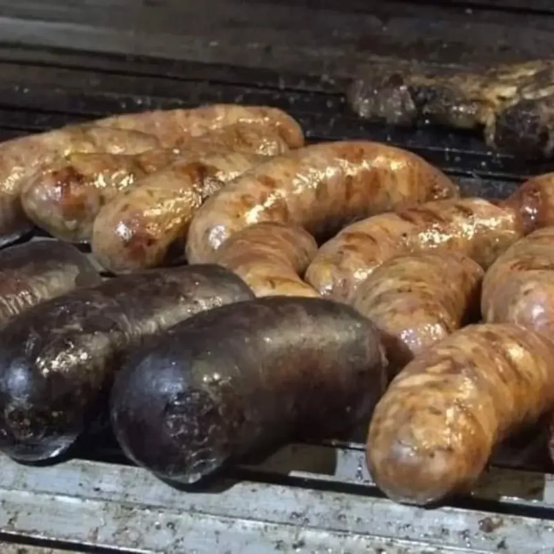 Salchichas a la parrilla, algunas negras, otras marrones, sobre una parrilla de metal.