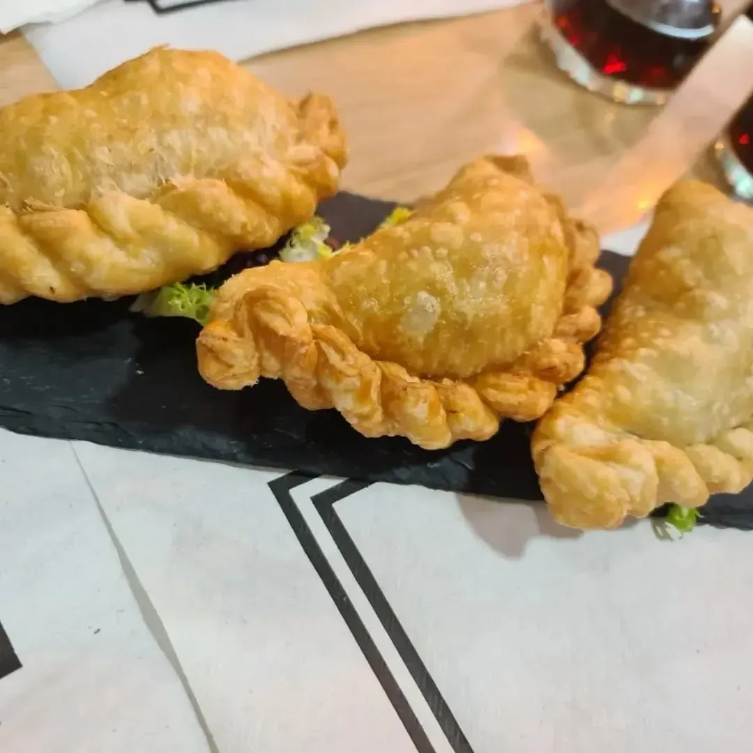 Tres empanadas doradas sobre una pizarra negra, servidas sobre papel blanco.