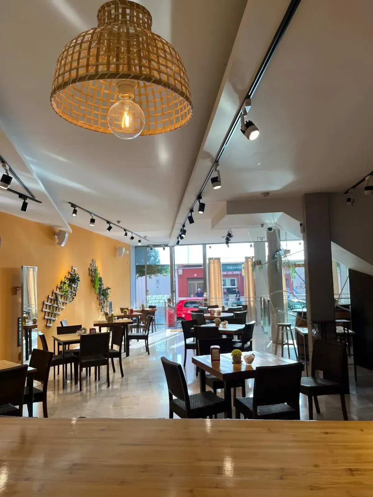 Interior de restaurante con mesas y sillas, lámparas decorativas y vista a la calle exterior.