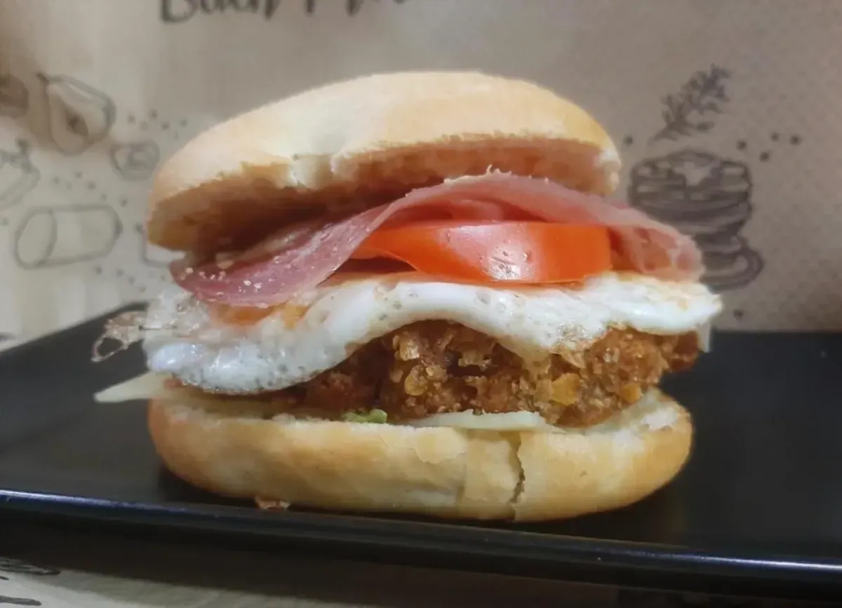 Hamburguesa con huevo frito, tocino, tomate y hamburguesa en un pan, colocada en un plato negro.