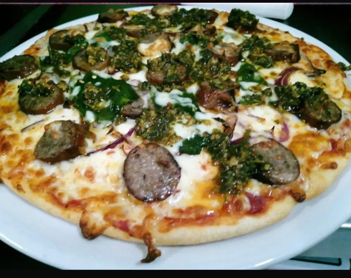 Pizza con salchicha, pesto y cebolla roja en un plato blanco.