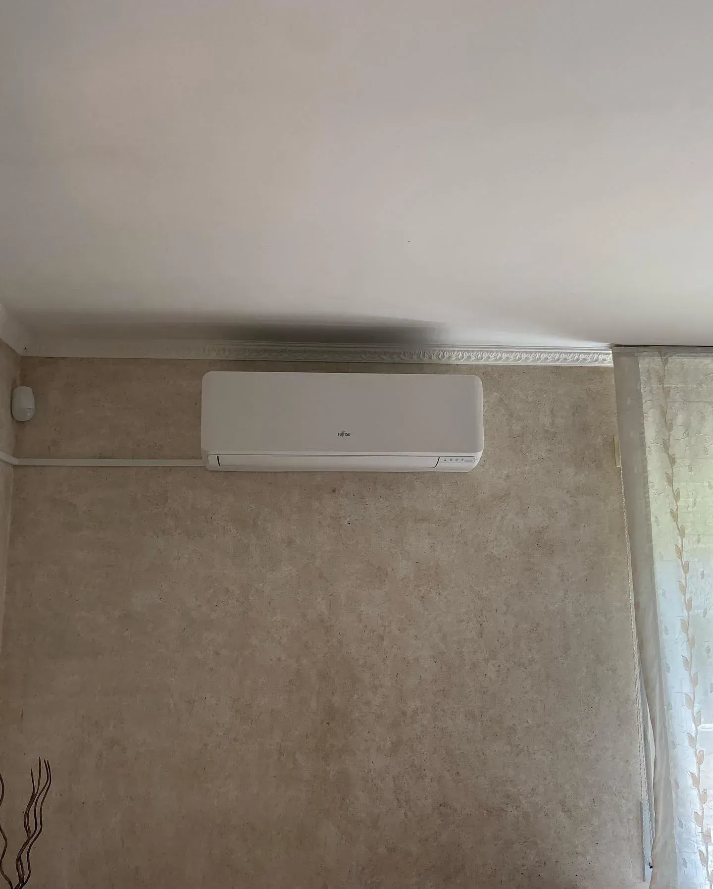 Aire acondicionado blanco de pared, instalado cerca del techo sobre una pared beige.