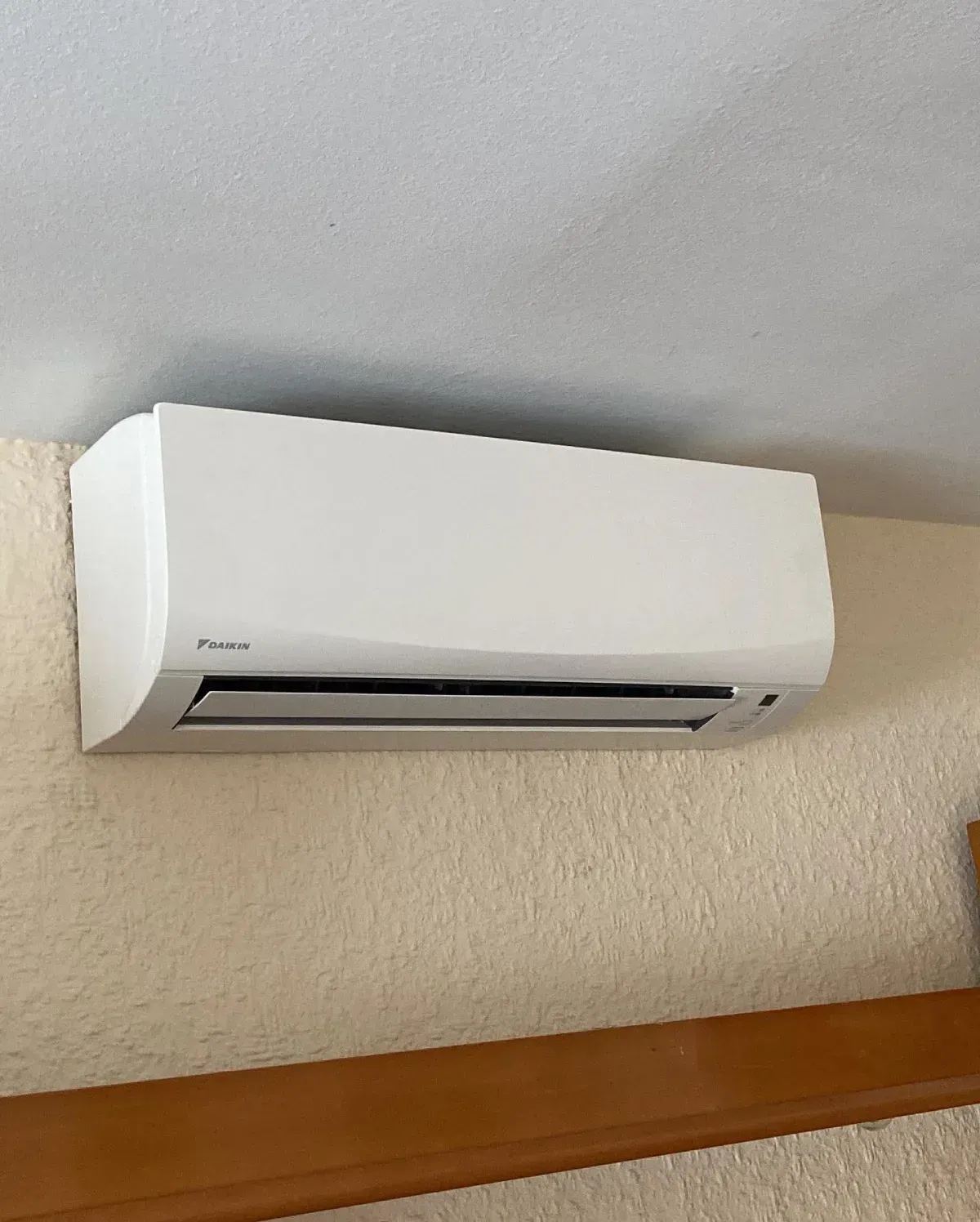 Aire acondicionado blanco montado en la pared, sobre una moldura de madera en una pared beige.