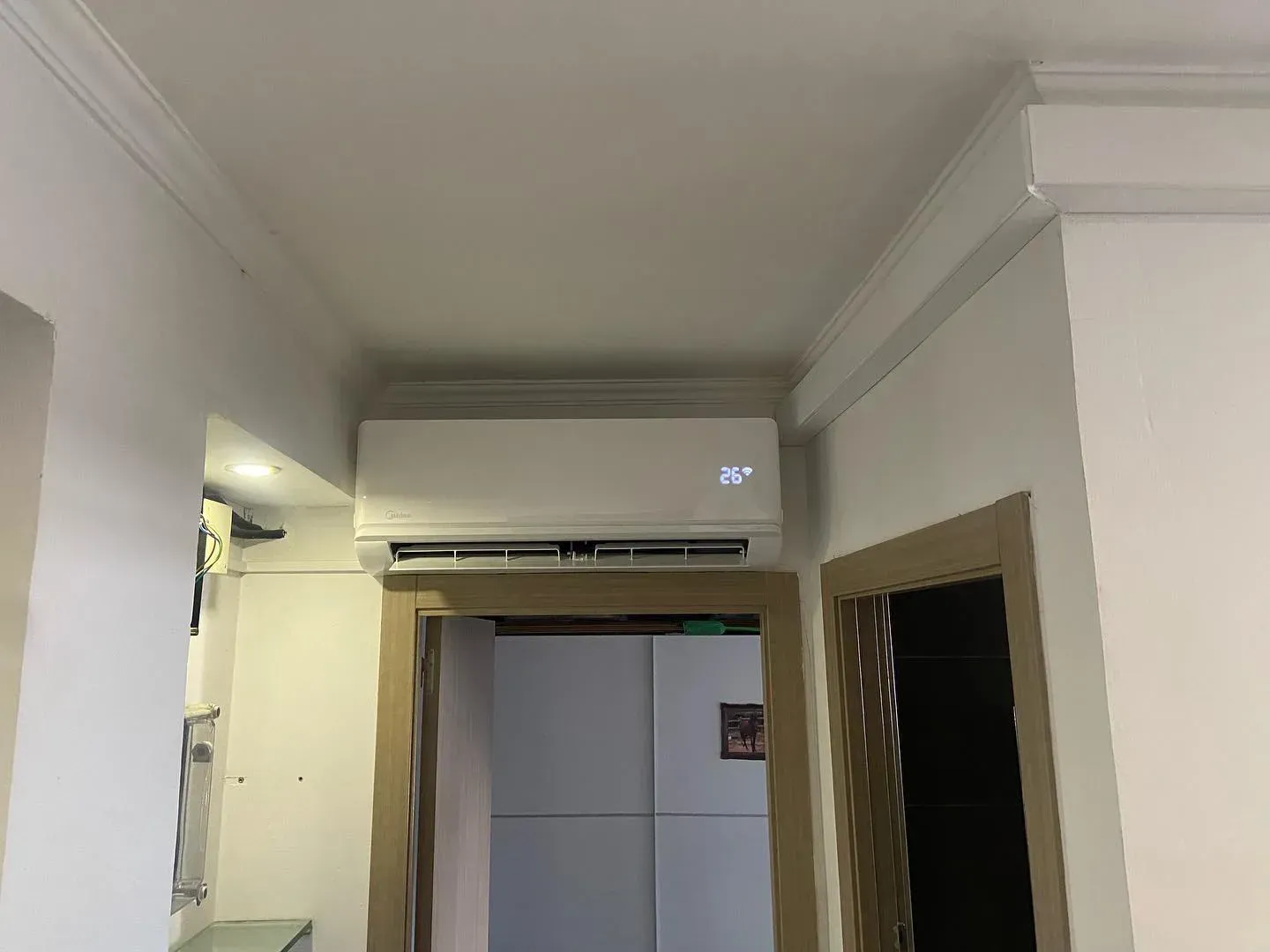 Pasillo con un aire acondicionado montado en la pared, encima de una puerta abierta que da a una cocina o habitación