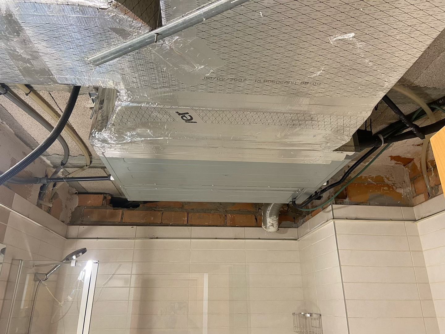 Conductos de climatización a la vista sobre una ducha alicatada, con manchas de agua en el techo.