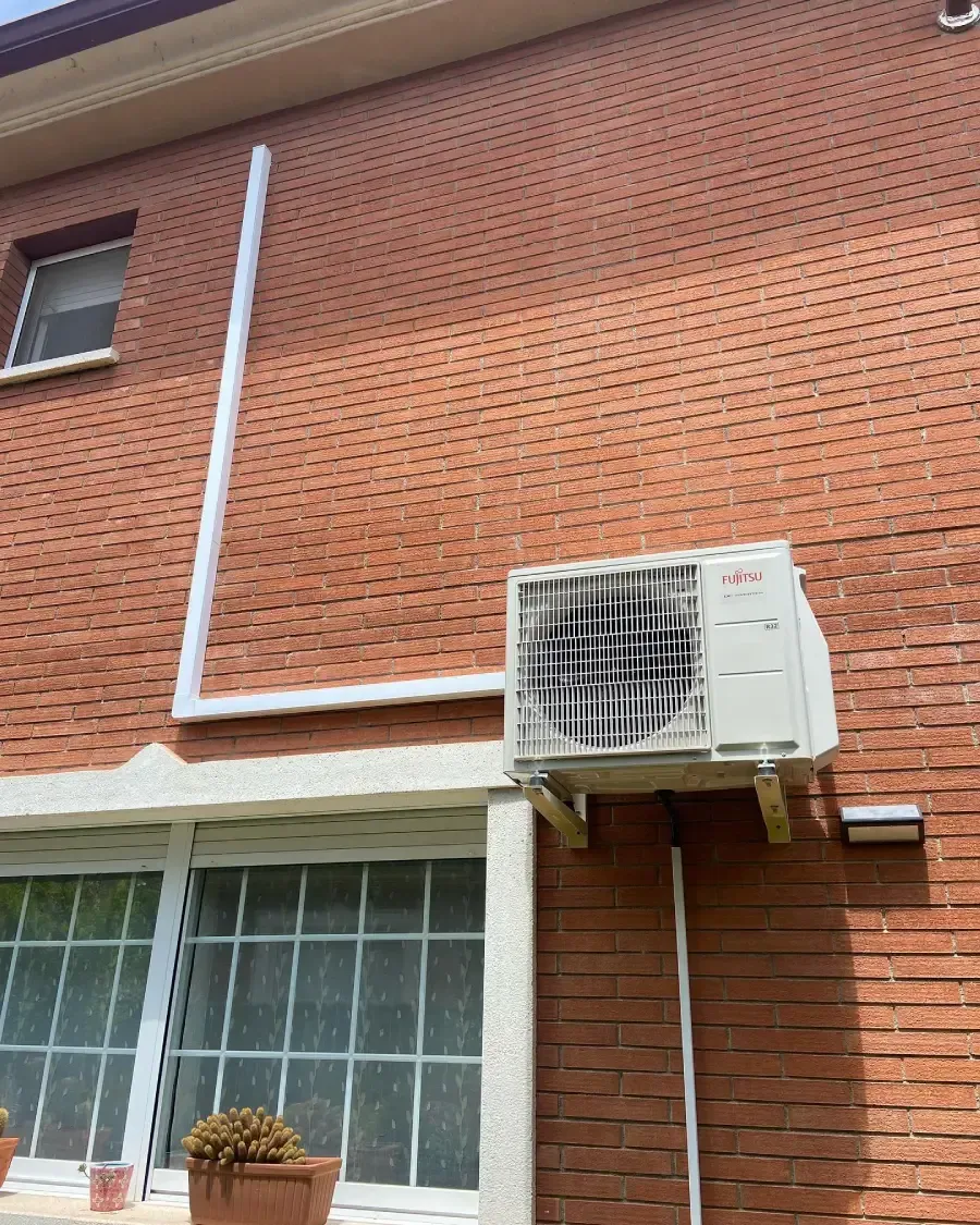 Exterior de un edificio de ladrillo con una ventana, una tubería blanca y un aire acondicionado montado en la pared
