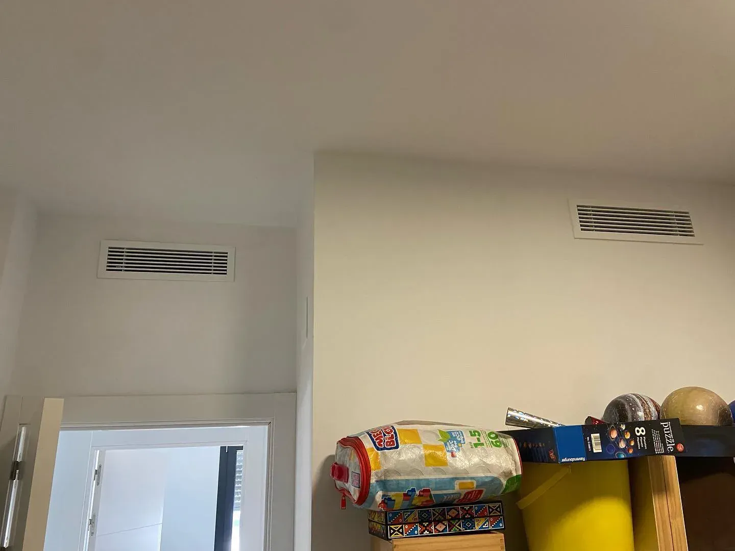 Esquina interior de una habitación con dos rejillas de ventilación en la pared, encima de una puerta