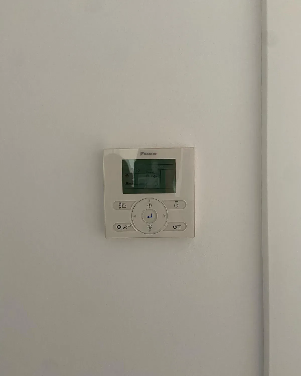 Pared blanca con un pequeño panel de control digital del termostato instalado cerca de una esquina.