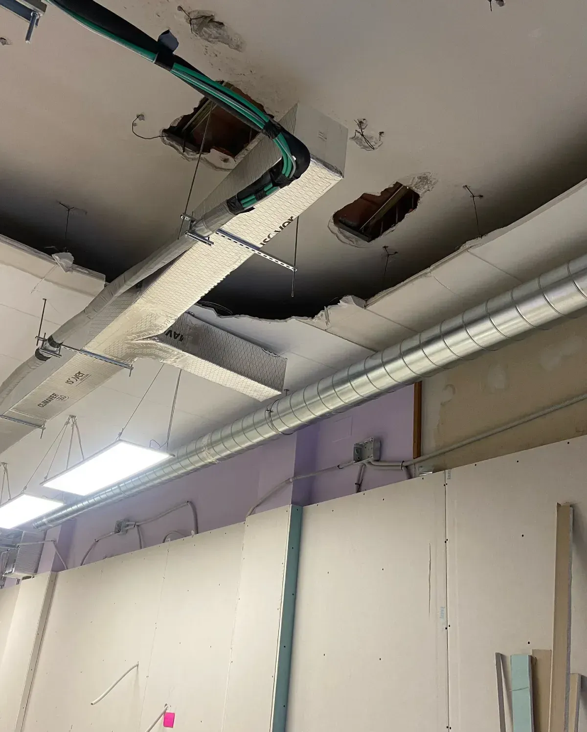 Techo dañado, con grandes agujeros, cables expuestos y paneles rotos en una habitación con luces fluorescentes.