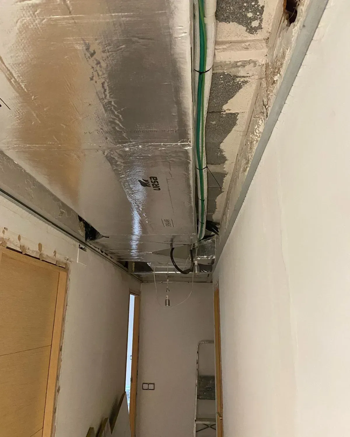 Techo dañado, con el aislamiento y las tuberías al descubierto, en un pasillo estrecho en reparación