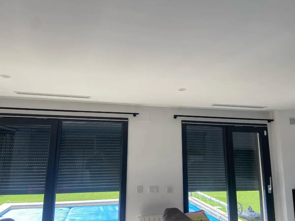 Interior de una habitación con dos ventanas oscuras con contraventanas y vistas a un estadio en el exterior