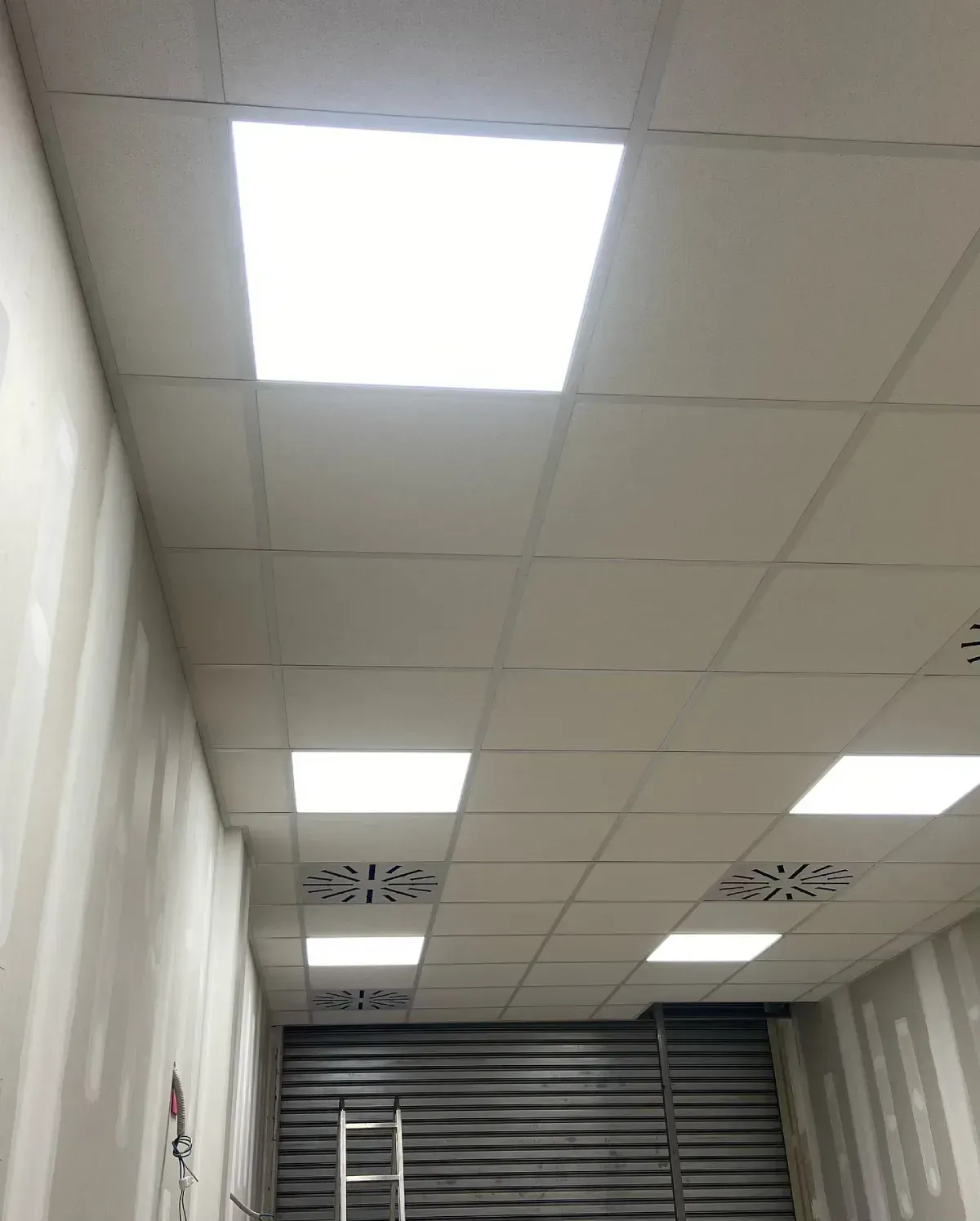 Techo del pasillo con paneles fluorescentes brillantes y una escalera al fondo
