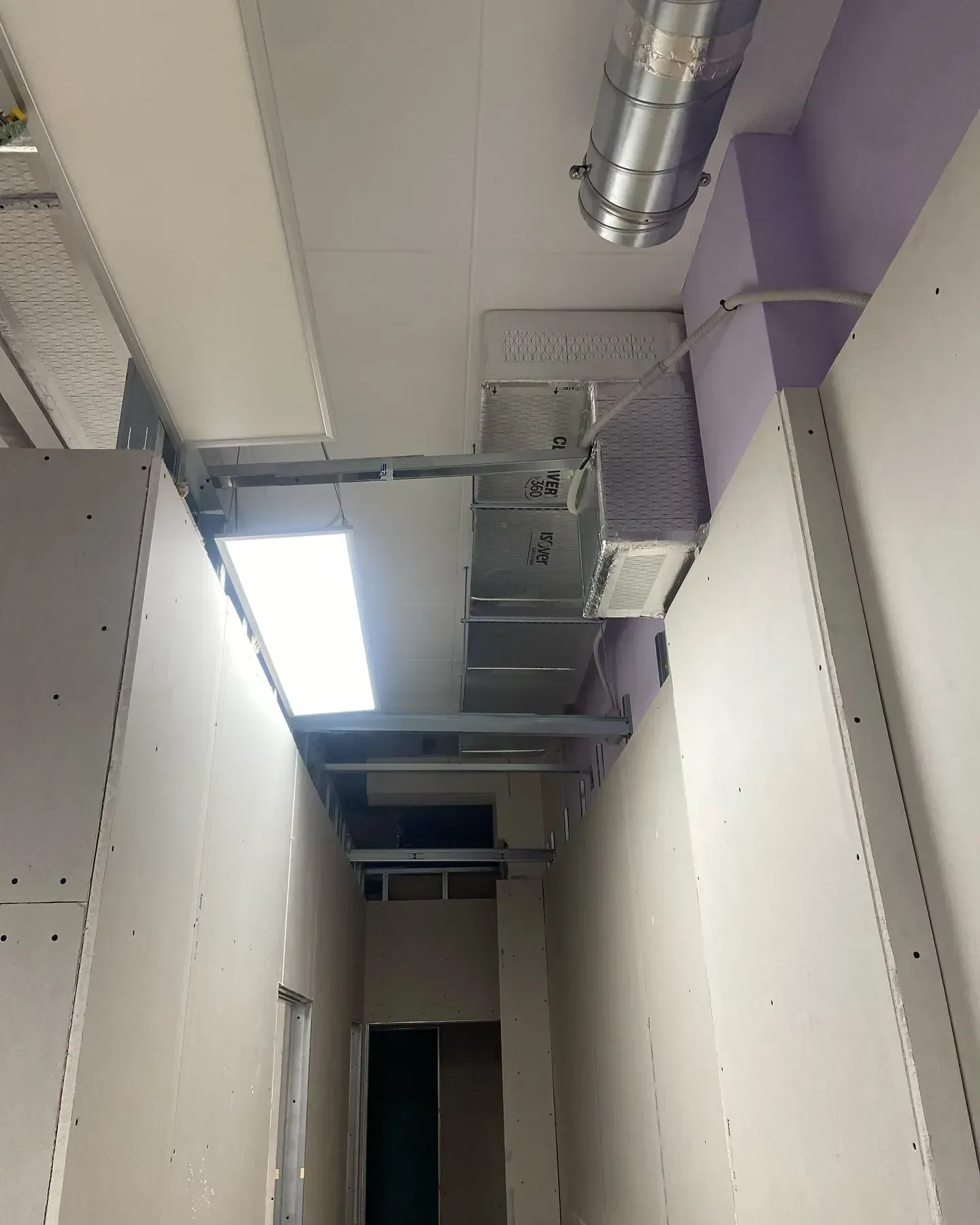 Techo de un pasillo estrecho con conductos y rejillas de ventilación a la vista, y un panel de claraboya muy luminoso.