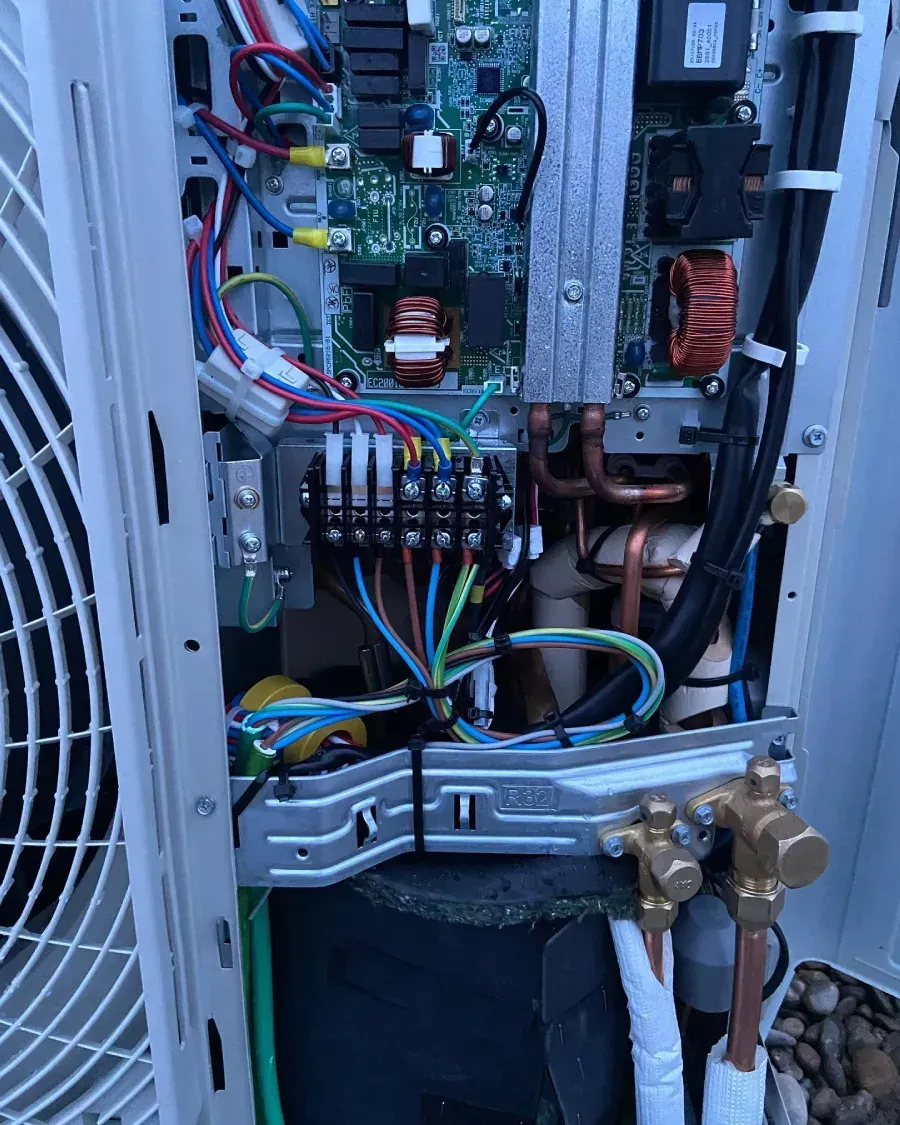 Panel de control eléctrico abierto con cableado, placas de circuito, bobinas de cobre y tuberías conectadas.