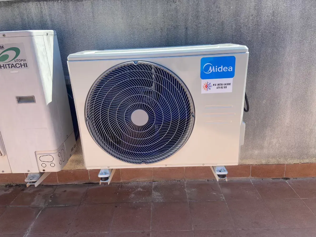 Unidad exterior de aire acondicionado Midea con un gran ventilador, montada en la pared sobre un suelo de baldosas
