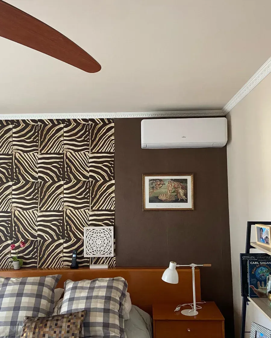 Dormitorio con arte mural estampado, aire acondicionado de pared, cuadro enmarcado y lámpara de noche junto a una cama
